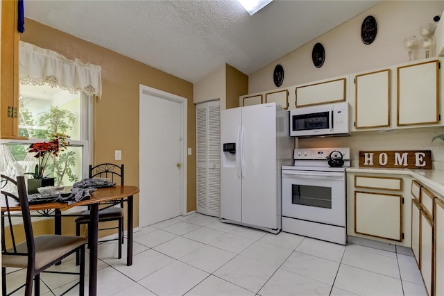 kitchen with cream cabinets, vaulted ceiling, a textured ceiling, white appliances, and light tile patterned floors