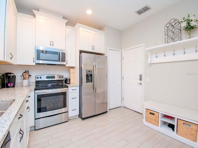 kitchen featuring light stone countertops, white cabinetry, appliances with stainless steel finishes, and light wood-type flooring