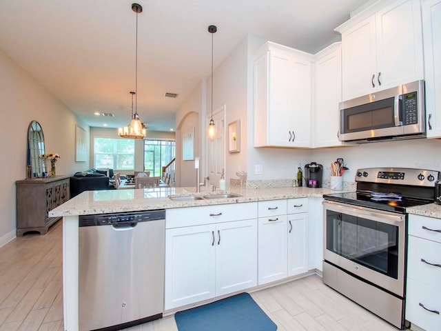 kitchen with sink, appliances with stainless steel finishes, kitchen peninsula, pendant lighting, and white cabinets