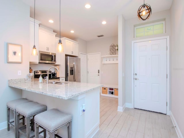 kitchen featuring white cabinetry, a breakfast bar, light stone countertops, appliances with stainless steel finishes, and sink