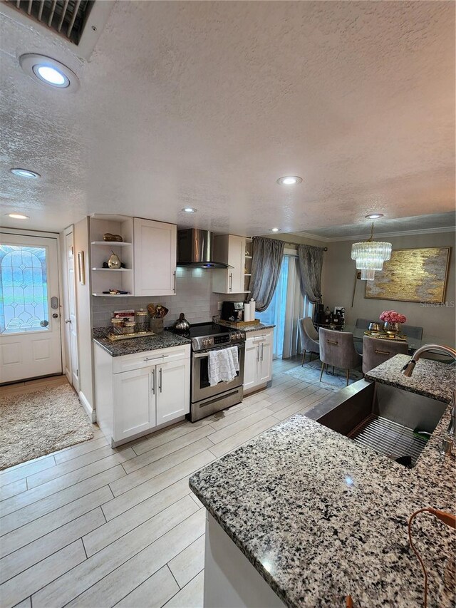 kitchen with wall chimney range hood, stainless steel electric stove, white cabinets, dark stone countertops, and a textured ceiling