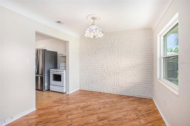 unfurnished dining area featuring brick wall, plenty of natural light, and hardwood / wood-style floors