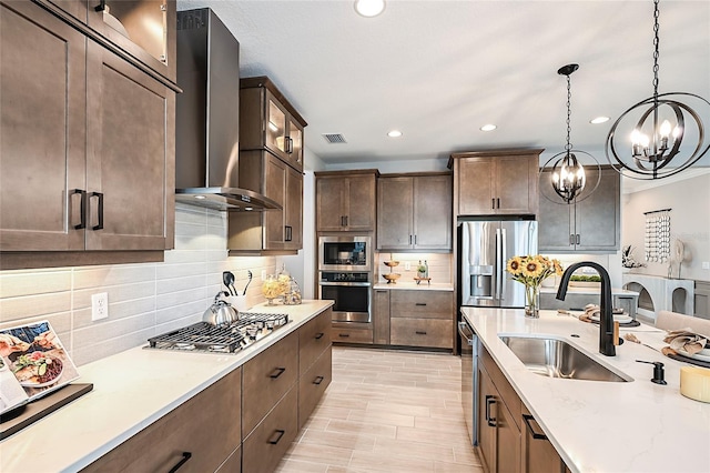 kitchen with appliances with stainless steel finishes, sink, decorative backsplash, a notable chandelier, and wall chimney exhaust hood