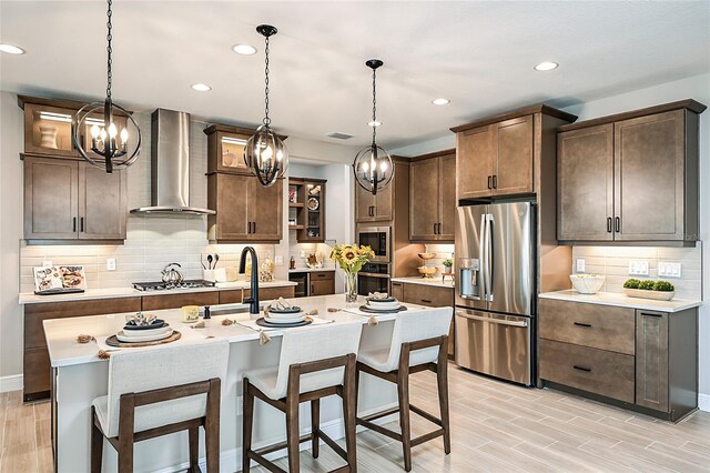 kitchen with decorative backsplash, wall chimney exhaust hood, appliances with stainless steel finishes, and an island with sink