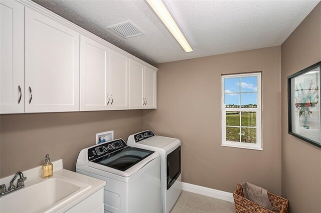 laundry room with washing machine and clothes dryer, sink, cabinets, light tile patterned floors, and a textured ceiling