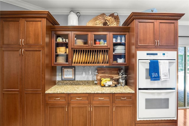 kitchen featuring hardwood / wood-style flooring, white double oven, light stone countertops, and crown molding