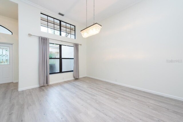 spare room with an inviting chandelier, light hardwood / wood-style floors, and a towering ceiling