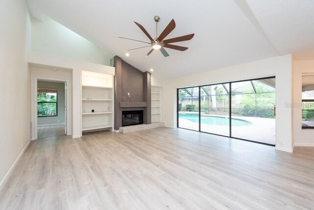 unfurnished living room featuring a fireplace, ceiling fan, built in shelves, high vaulted ceiling, and light hardwood / wood-style flooring