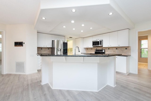 kitchen with appliances with stainless steel finishes, tasteful backsplash, white cabinets, a kitchen island with sink, and light wood-type flooring