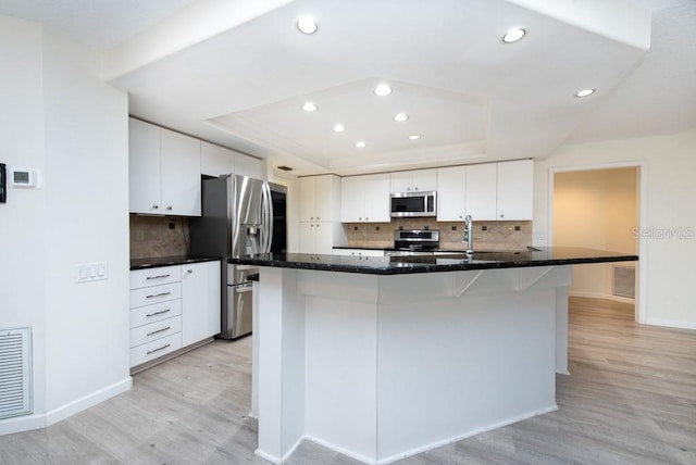 kitchen featuring tasteful backsplash, stainless steel appliances, light hardwood / wood-style floors, and white cabinets