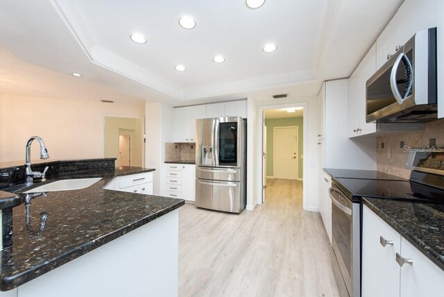 kitchen with dark stone counters, stainless steel appliances, sink, backsplash, and a raised ceiling