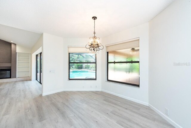 unfurnished dining area with a notable chandelier, a fireplace, built in shelves, and light wood-type flooring