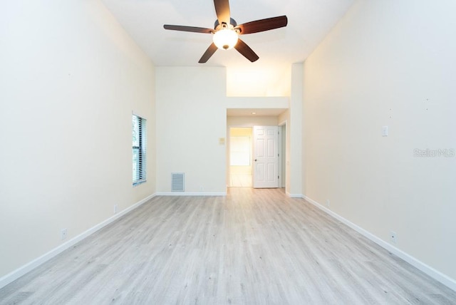 empty room with a towering ceiling, light wood-type flooring, and ceiling fan