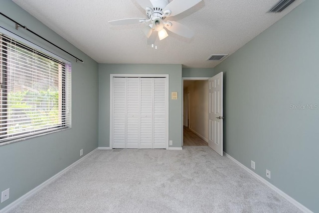 unfurnished bedroom featuring a textured ceiling, a closet, carpet floors, and ceiling fan