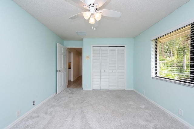 unfurnished bedroom with a textured ceiling, light colored carpet, a closet, and ceiling fan