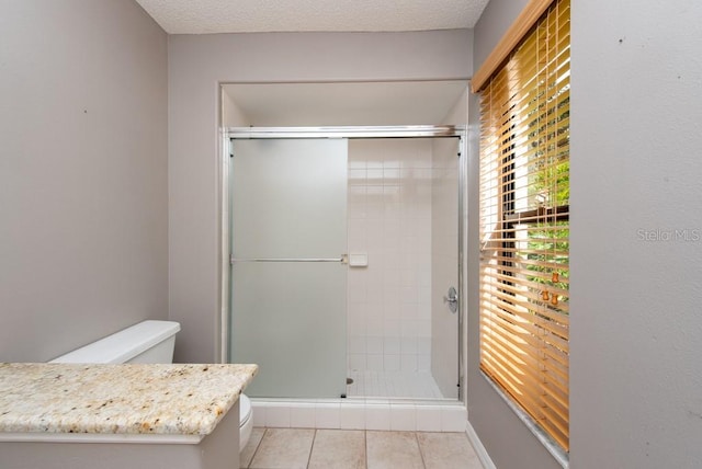 bathroom featuring tile patterned flooring, a shower with door, toilet, and a textured ceiling