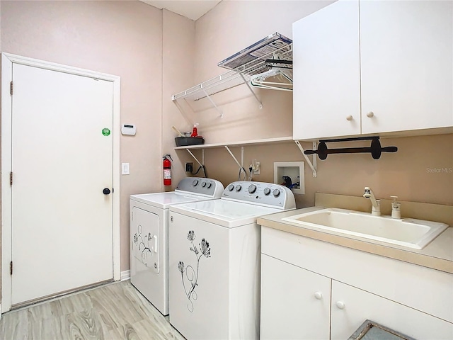 clothes washing area with light wood-type flooring, cabinet space, a sink, and independent washer and dryer