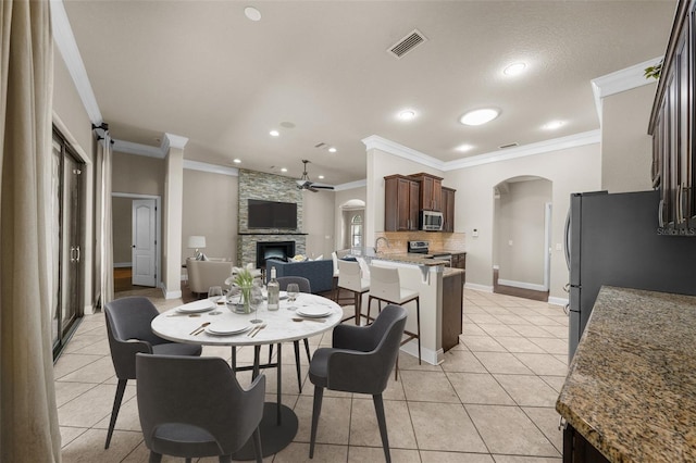 tiled dining area featuring ornamental molding, a textured ceiling, and a stone fireplace