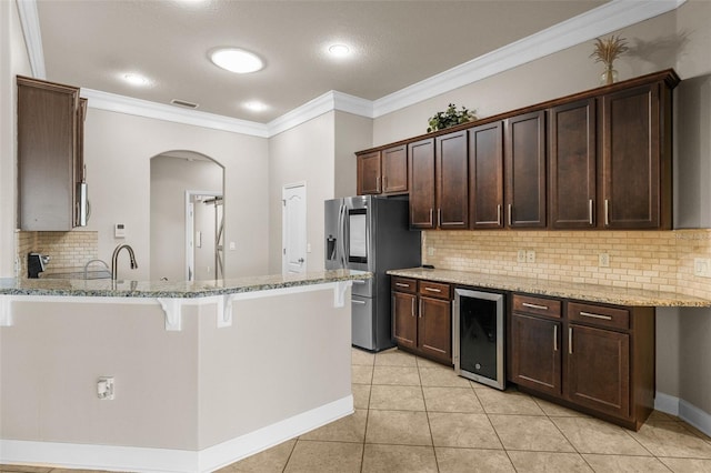 kitchen with light tile patterned floors, beverage cooler, backsplash, light stone countertops, and a kitchen breakfast bar