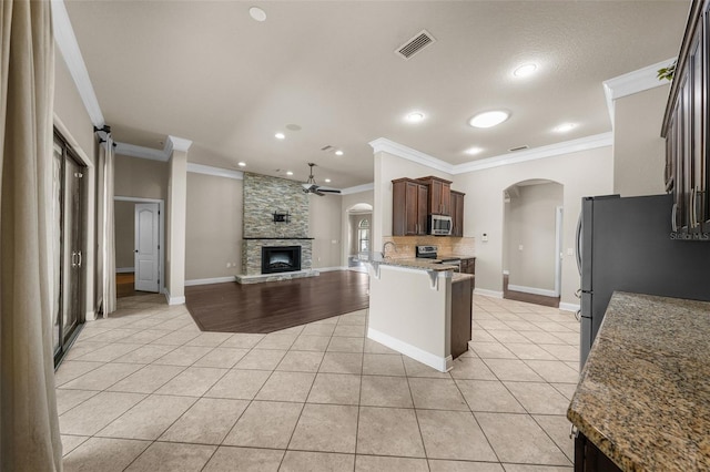 kitchen featuring tasteful backsplash, light tile patterned floors, kitchen peninsula, appliances with stainless steel finishes, and a fireplace