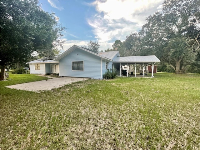 rear view of house with metal roof, a lawn, and concrete driveway