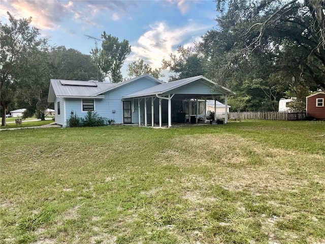 back of property with an attached carport, fence, metal roof, and a lawn