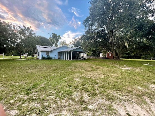 view of yard featuring a storage shed, an outbuilding, fence, and a sunroom