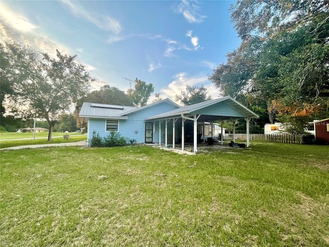 rear view of property featuring metal roof, a yard, a carport, and fence