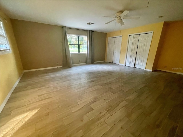 unfurnished bedroom featuring ceiling fan, multiple closets, and light hardwood / wood-style floors