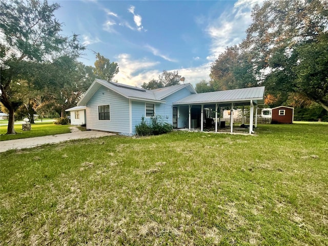 rear view of property with a storage shed, metal roof, a lawn, and an outbuilding