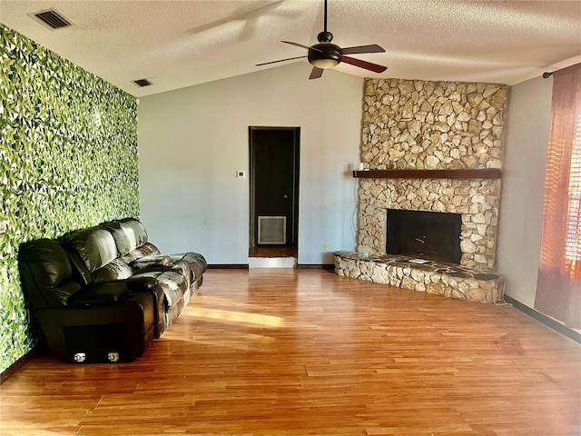 living area featuring vaulted ceiling, a stone fireplace, light wood-style flooring, and visible vents