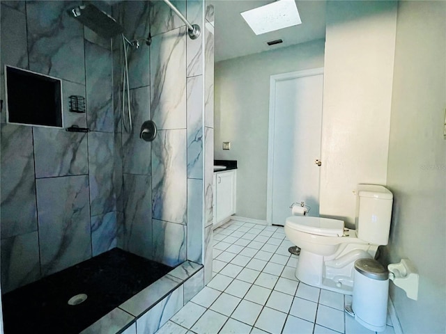 bathroom with a skylight, vanity, tiled shower, tile patterned floors, and toilet