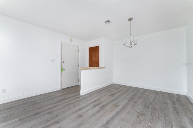 spare room with an inviting chandelier and wood-type flooring