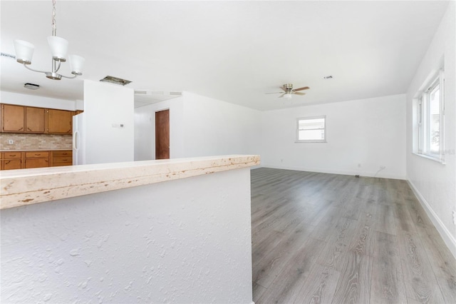 unfurnished living room featuring plenty of natural light, ceiling fan with notable chandelier, and light hardwood / wood-style floors