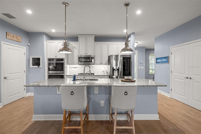 kitchen with light stone counters, stainless steel appliances, white cabinets, and a center island with sink