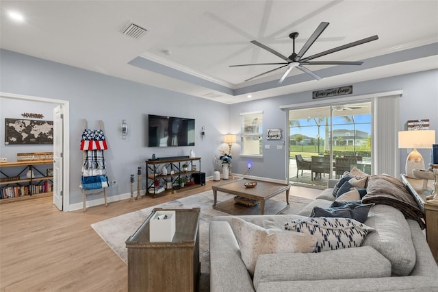 living room featuring ceiling fan, ornamental molding, a tray ceiling, and light hardwood / wood-style flooring