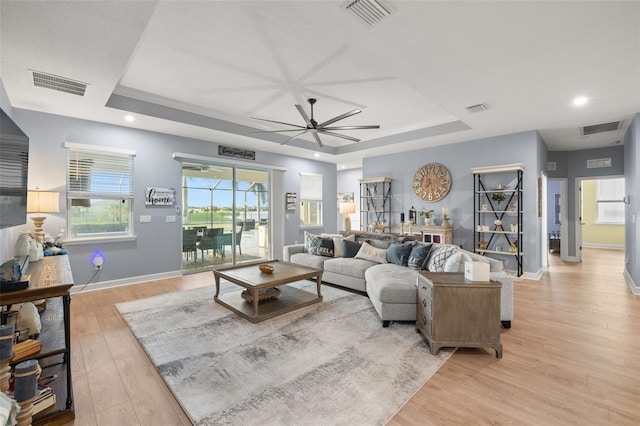 living room with a raised ceiling, ceiling fan, and light hardwood / wood-style flooring