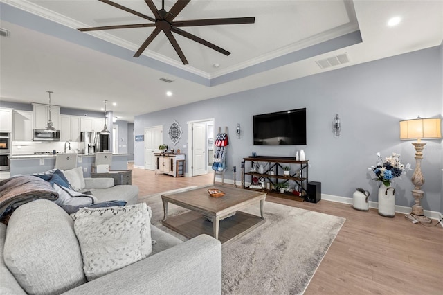 living room with ornamental molding, light hardwood / wood-style flooring, ceiling fan, and a tray ceiling