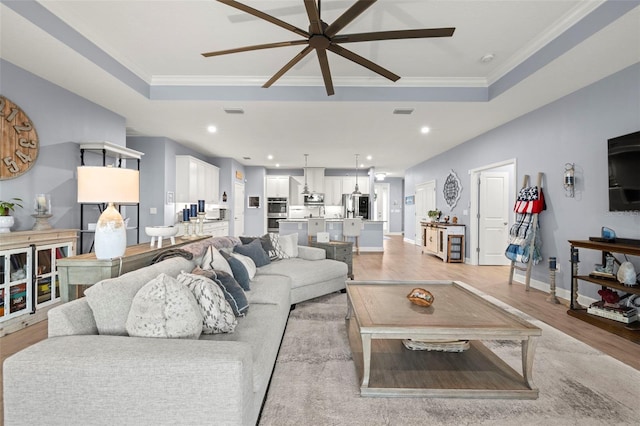 living room with ceiling fan, ornamental molding, a tray ceiling, and light wood-type flooring