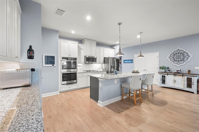 kitchen featuring light stone counters, white cabinetry, decorative light fixtures, appliances with stainless steel finishes, and backsplash