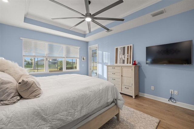 bedroom with crown molding, a tray ceiling, ceiling fan, and light wood-type flooring