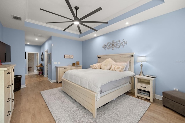 bedroom with ceiling fan, ornamental molding, a tray ceiling, and light hardwood / wood-style floors