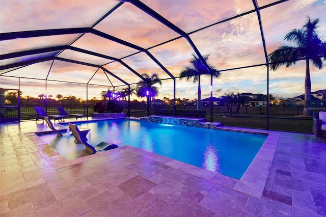 pool at dusk with pool water feature, glass enclosure, and a patio area