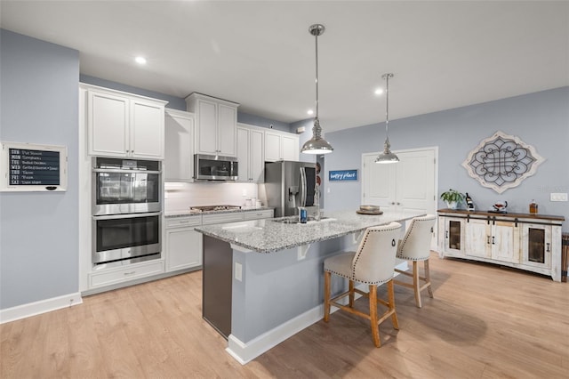 kitchen featuring appliances with stainless steel finishes, pendant lighting, light stone countertops, a kitchen island with sink, and white cabinets