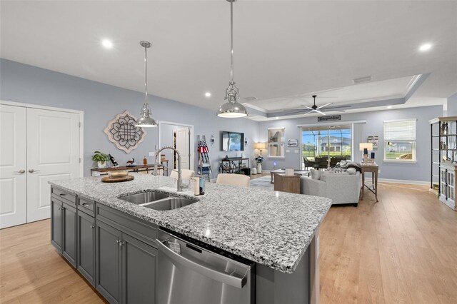 kitchen with decorative light fixtures, sink, a kitchen island with sink, stainless steel dishwasher, and a tray ceiling