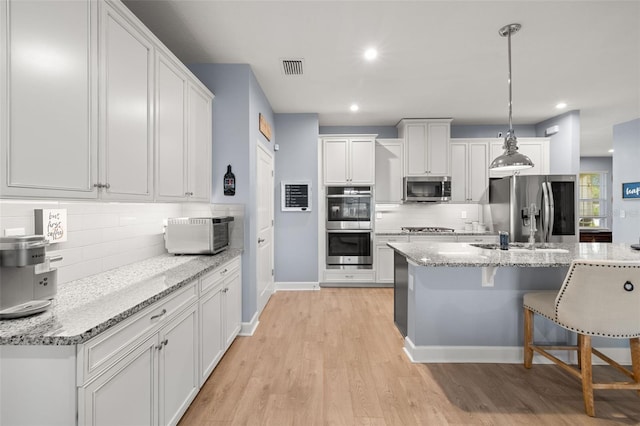 kitchen featuring appliances with stainless steel finishes, decorative light fixtures, white cabinetry, light stone countertops, and light wood-type flooring