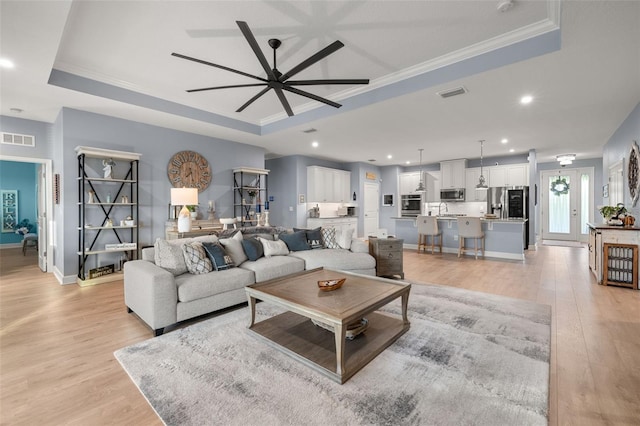 living room featuring light hardwood / wood-style flooring, ornamental molding, and a raised ceiling