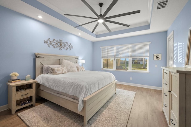 bedroom with crown molding, a tray ceiling, light hardwood / wood-style flooring, and ceiling fan