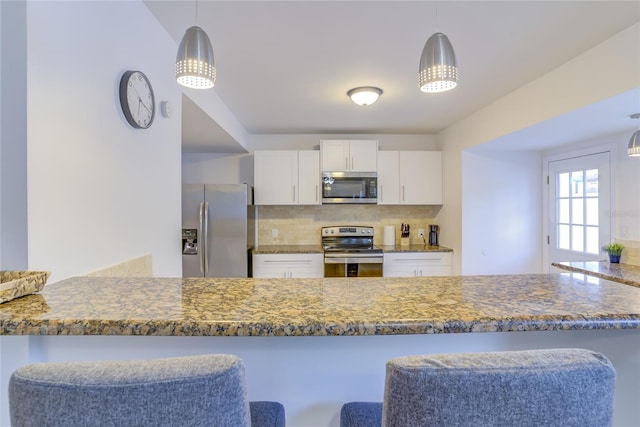 kitchen featuring tasteful backsplash, white cabinets, dark stone counters, stainless steel appliances, and a kitchen bar