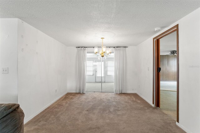 carpeted spare room with a notable chandelier and a textured ceiling